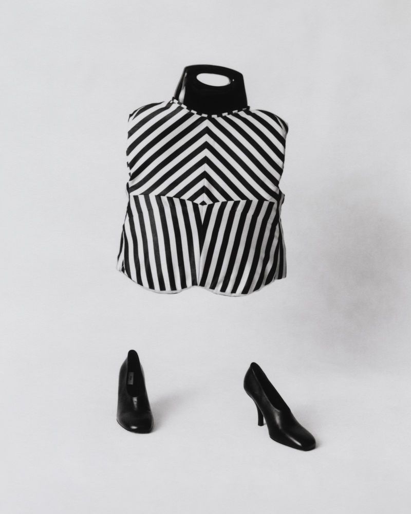 Black and white striped top on a mannequin stand with black high heels on a white background in a studio setting, fashion shot.