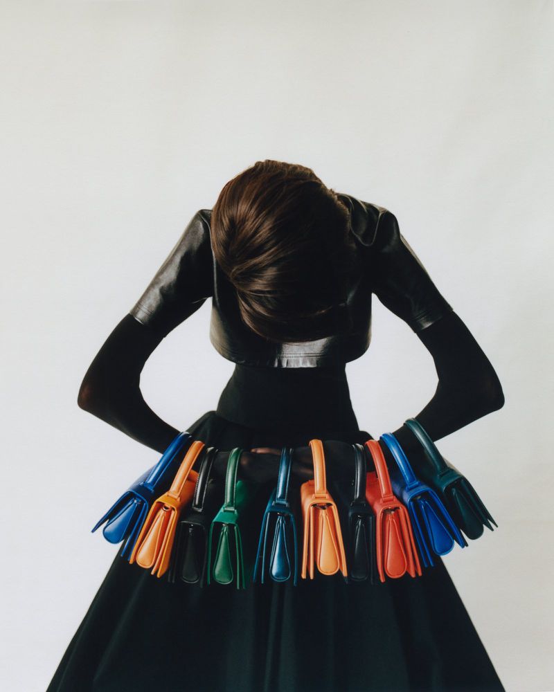 Woman in black fashion holding colorful purses on waistband against white background. Fashion editorial photograph of purses.