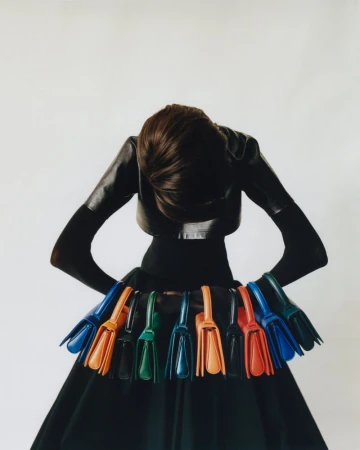 Woman in black fashion holding colorful purses on waistband against white background. Fashion editorial photograph of purses.