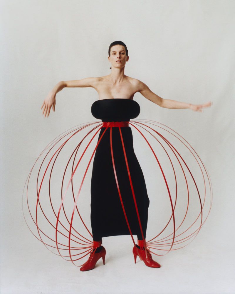 Fashion photography: Woman in black dress with red accents poses in a photo studio with a minimalist white backdrop, showcasing creative styling.
