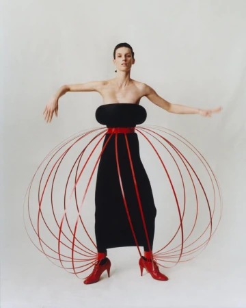 Fashion photography: Woman in black dress with red accents poses in a photo studio with a minimalist white backdrop, showcasing creative styling.