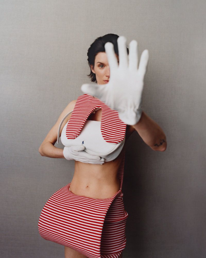 Adult female poses with a white glove held up to the camera obscuring her face, wearing a red and white striped garment.