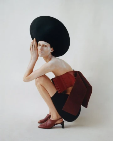 Model Marte Mei van Haaster in a large black hat and red top squatting against a plain white background for M Le magazine du Monde