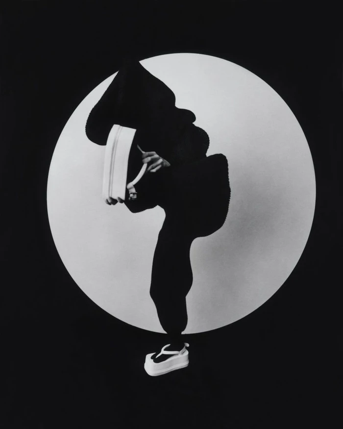 Model in silhouette wearing dark apparel and white platform shoes against a circular white backdrop for M Le magazine du Monde