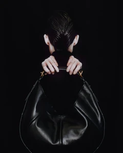 Model holding large black leather hobo bag in front of face against dark background for M Le magazine du Monde editorial project UNE PARADE DADA