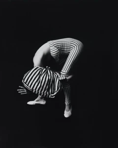 Model in striped bodysuit bending backwards against a black background wearing white flats