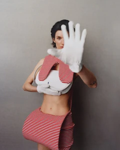 Model Marte Mei van Haaster wearing a striped red-and-white outfit with white gloves held up in a gesture for M Le magazine du Monde.