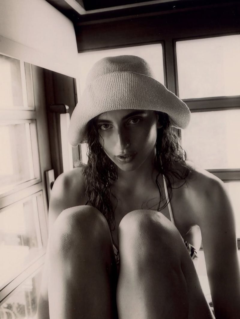 Monochrome portrait of a woman wearing a hat, sitting indoors, featuring soft window light and a vintage-style aesthetic.