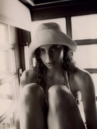 Monochrome portrait of a woman wearing a hat, sitting indoors, featuring soft window light and a vintage-style aesthetic.