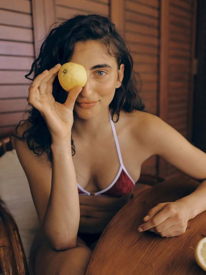 Woman in a burgundy bikini holding a yellow lemon over her eye for Vogue Greece photographed by Hein Gijsbers.