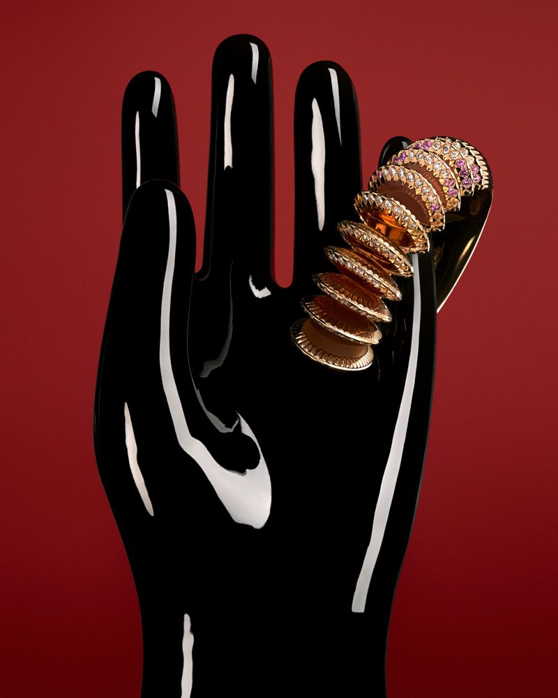 Gold ring with gemstones on a glossy black mannequin hand, red studio backdrop, jewelry advertisement, high contrast product photography.