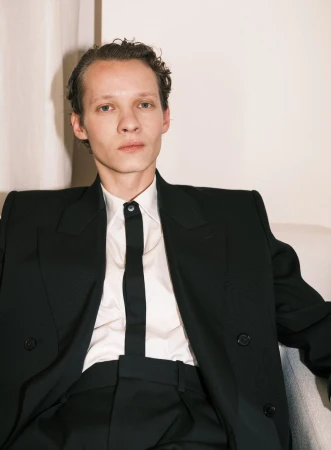 Felix Kammerer seated wearing a tailored black suit jacket and white shirt with a skinny black tie