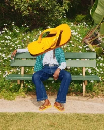 Surreal fashion image for Havaianas featuring a person sitting on a park bench with a giant yellow flip flop replacing their head