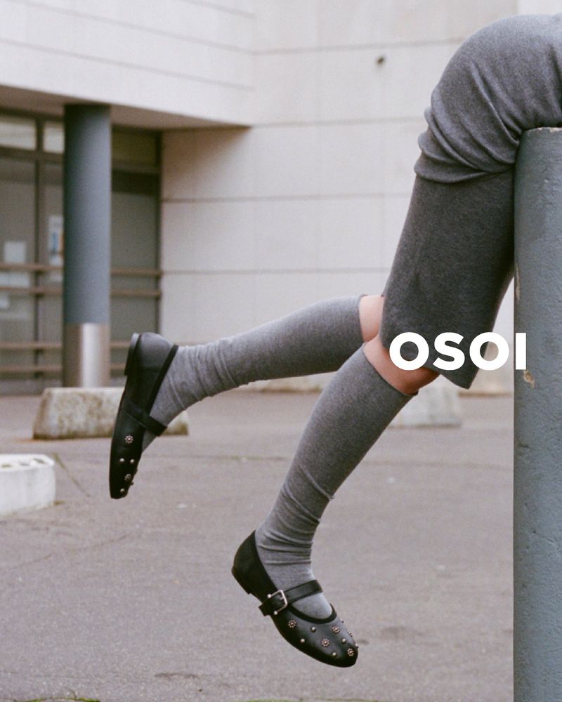 Fashion shot of woman's legs wearing gray socks and black Mary Jane shoes, sitting on concrete post in urban environment, OSOI logo visible.