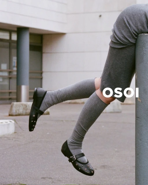 Fashion shot of woman's legs wearing gray socks and black Mary Jane shoes, sitting on concrete post in urban environment, OSOI logo visible.