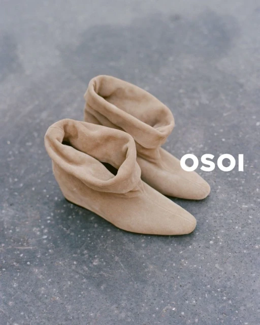 Tan-colored ankle boots with slouch detail on a grey textured surface, showcased in a fashion product shot.