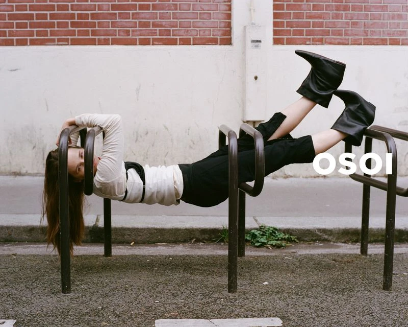 A fashion shot of a woman in a white shirt, black pants and black boots hanging upside down on a metal playground structure.