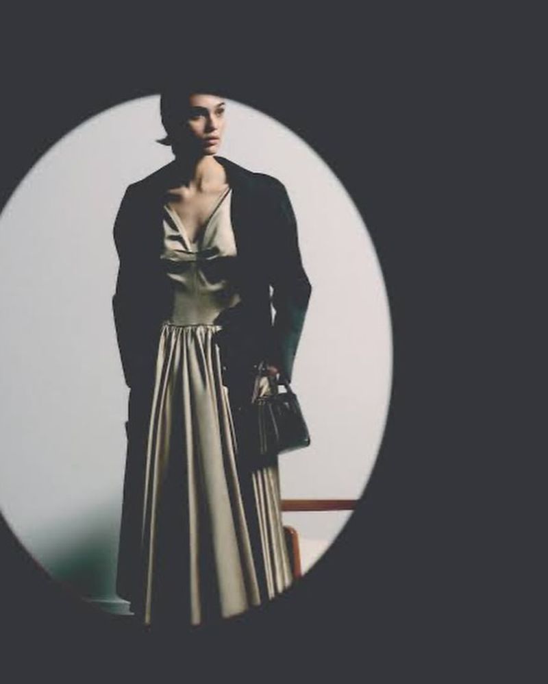 Model wearing a light dress and dark jacket holding a handbag framed inside an oval vignette for Prada Ramadan 2026.