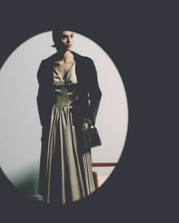 Model wearing a light dress and dark jacket holding a handbag framed inside an oval vignette for Prada Ramadan 2026.