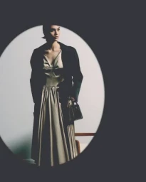 Model wearing a light dress and dark jacket holding a handbag framed inside an oval vignette for Prada Ramadan 2026.