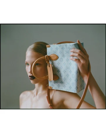 Model poses in a studio with a light blue Louis Vuitton box bag with tan leather trim and handle, featuring dark red lipstick.