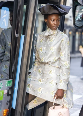 Stylish adult female in floral print shirt dress, dark tights, hat, and purse, standing on a bus with gray and blue accents.