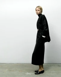 Model Lena Mantler wearing a black jacket and long skirt against a white studio background for 10 Magazine FACE VALUE editorial.