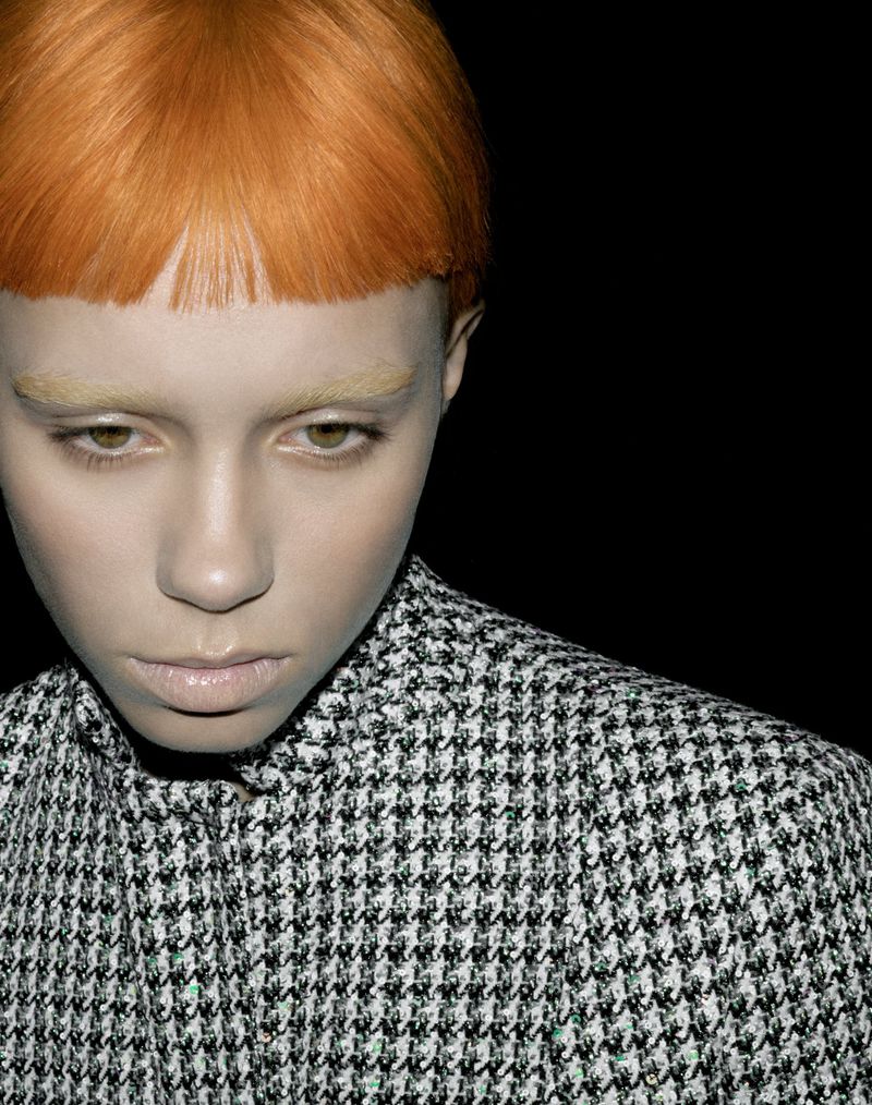 Close-up studio shot of a female model with orange hair and a houndstooth jacket against a dark background, emphasizing fashion and beauty.
