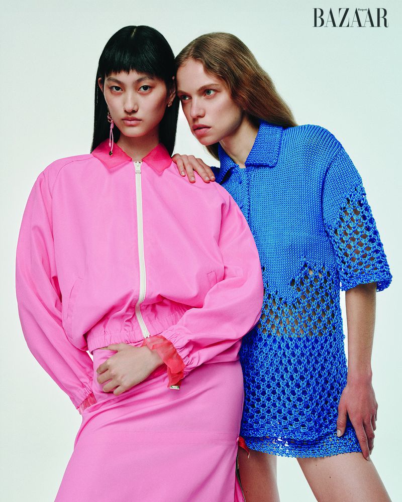Two fashion models pose in a photo studio wearing a pink jacket with a skirt and a blue crochet shirt for a Bazaar magazine editorial.