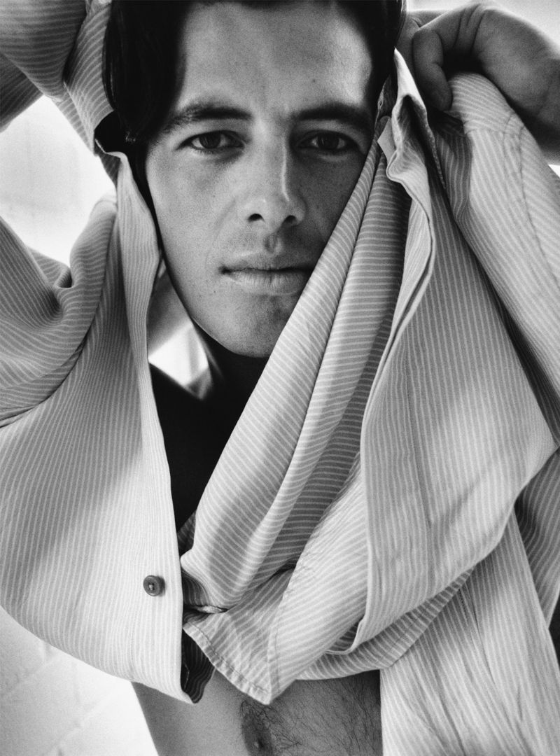 Black and white portrait of a man with dark hair and light skin, partially covered by a striped shirt, looking directly at the camera.