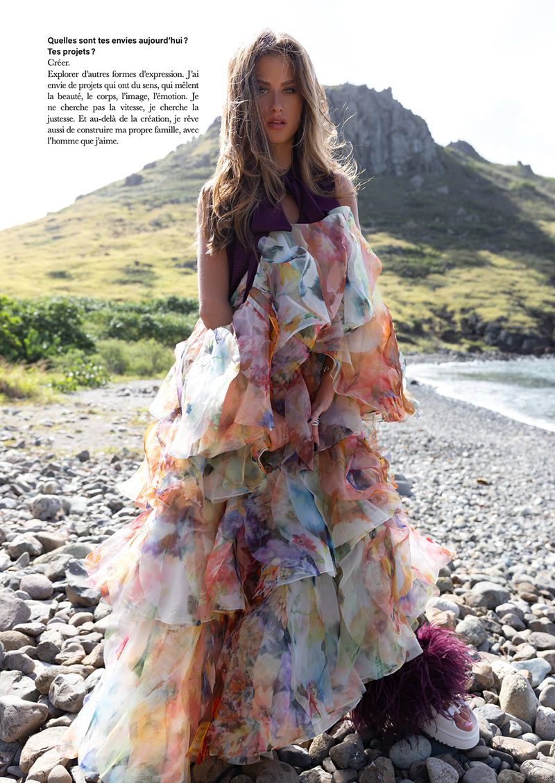 Model standing on a rocky beach wearing a voluminous floral dress and dark sleeveless top for Lui Magazine France.