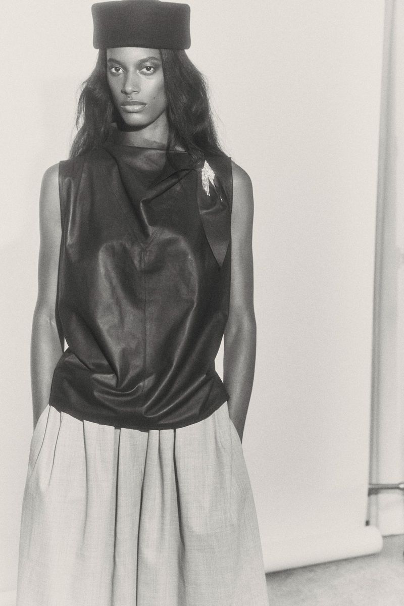 Monochrome studio fashion portrait of a Black model wearing a black tank top, neutral skirt, and hat against a white backdrop.