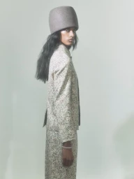 Model wearing a structured grey hat and patterned jacket against a neutral backdrop for M Le magazine du Monde editorial.