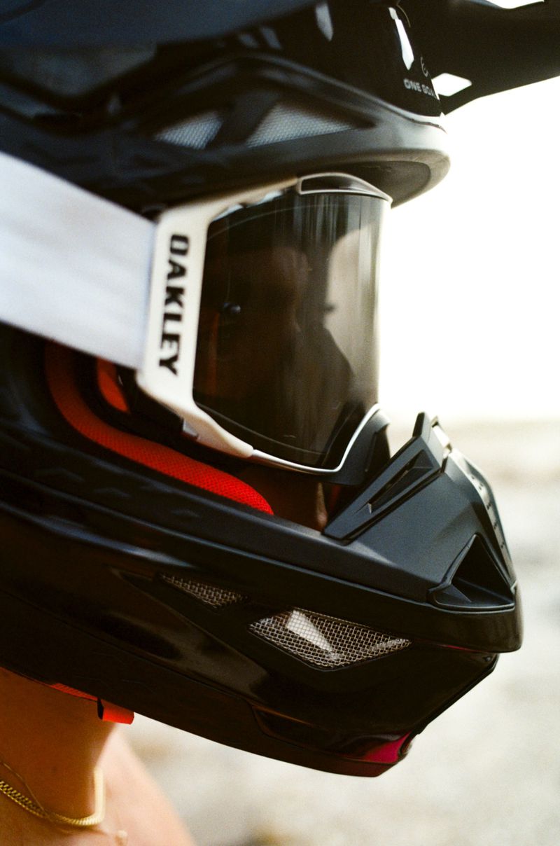 Close-up of a person wearing a black motocross helmet with goggles. The goggles have white straps and the helmet has a red accent.
