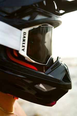 Close-up of a person wearing a black motocross helmet with goggles. The goggles have white straps and the helmet has a red accent.