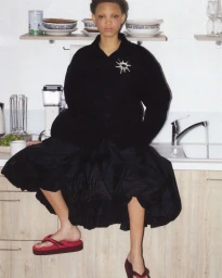 Model seated on a kitchen counter wearing a black shirt and red platform sandals with a silver star brooch