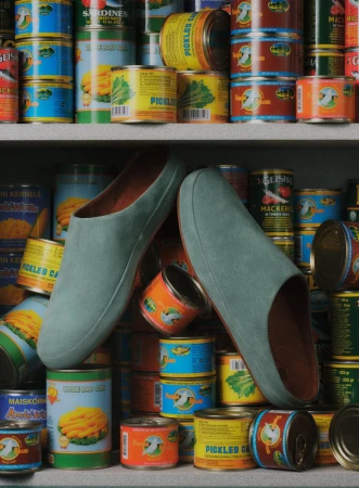 Indoor shot featuring a pair of indoor slippers resting among colorful stacks of canned food items displayed on shelves in a room.