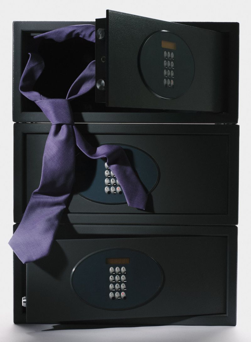 Stack of three black safes with digital keypads, the top safe open, with a purple necktie draped across the safes.