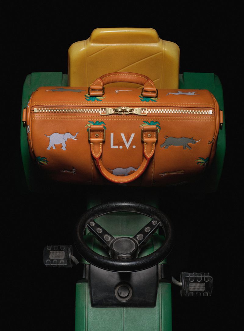 Fashion duffel bag with animal designs sits atop a green and yellow child's toy tractor in a studio setting against a black background.