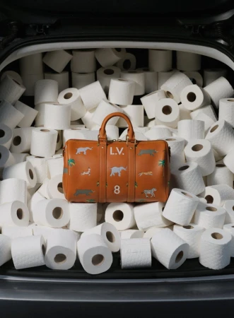 Tan leather duffel bag with animal designs surrounded by rolls of toilet paper, filling the rear cargo area of a car.