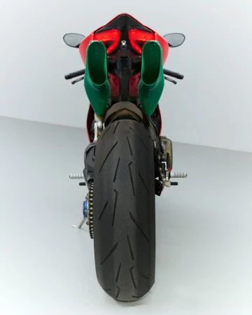 Back view of a red motorcycle with oversized green exhaust pipes against a white studio backdrop, highlighting the rear tire.