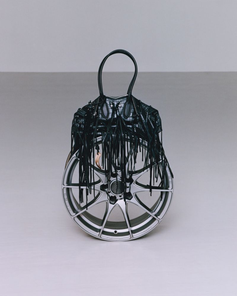 Fashion handbag constructed from fringed leather and repurposed as car wheel in a studio shot against a neutral background.