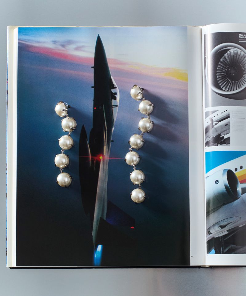 Pearl earrings on a magazine page with an airplane image. Jewelry advertisement with pearl drop earrings next to an aviation photo.