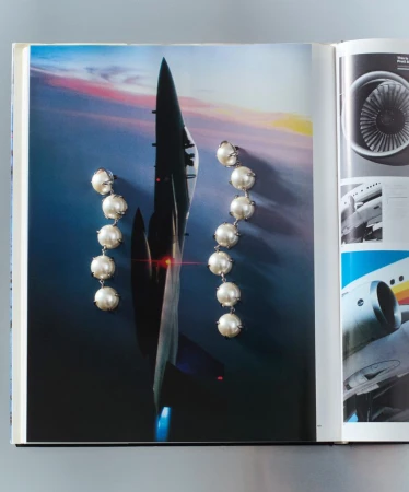 Pearl earrings on a magazine page with an airplane image. Jewelry advertisement with pearl drop earrings next to an aviation photo.