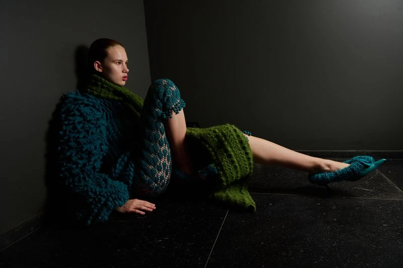 Fashion shot of a stylish adult woman in knit clothing posing indoors with a solid dark background, showcasing knit textures and studio lighting.