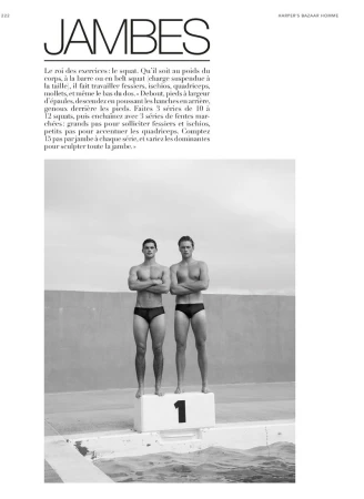 Two shirtless male athletes standing side-by-side with arms crossed atop a number-one podium by a swimming pool.
