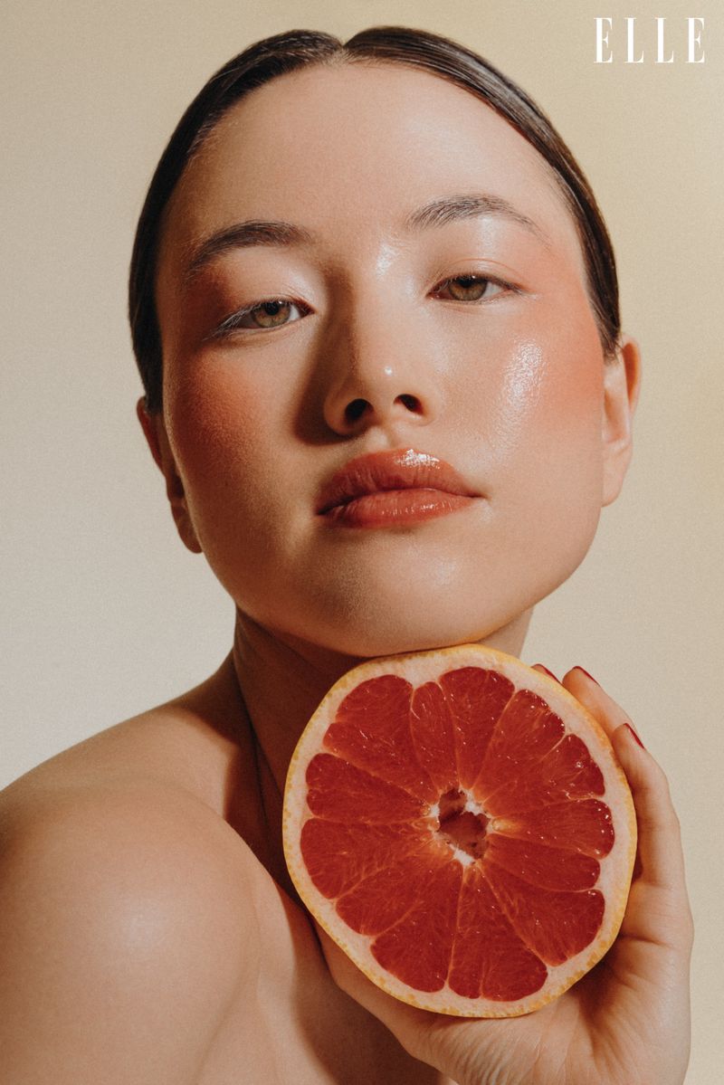 Close-up shot of an Asian woman holding a grapefruit, showcasing fresh beauty and skincare, with the 'ELLE' logo visible.