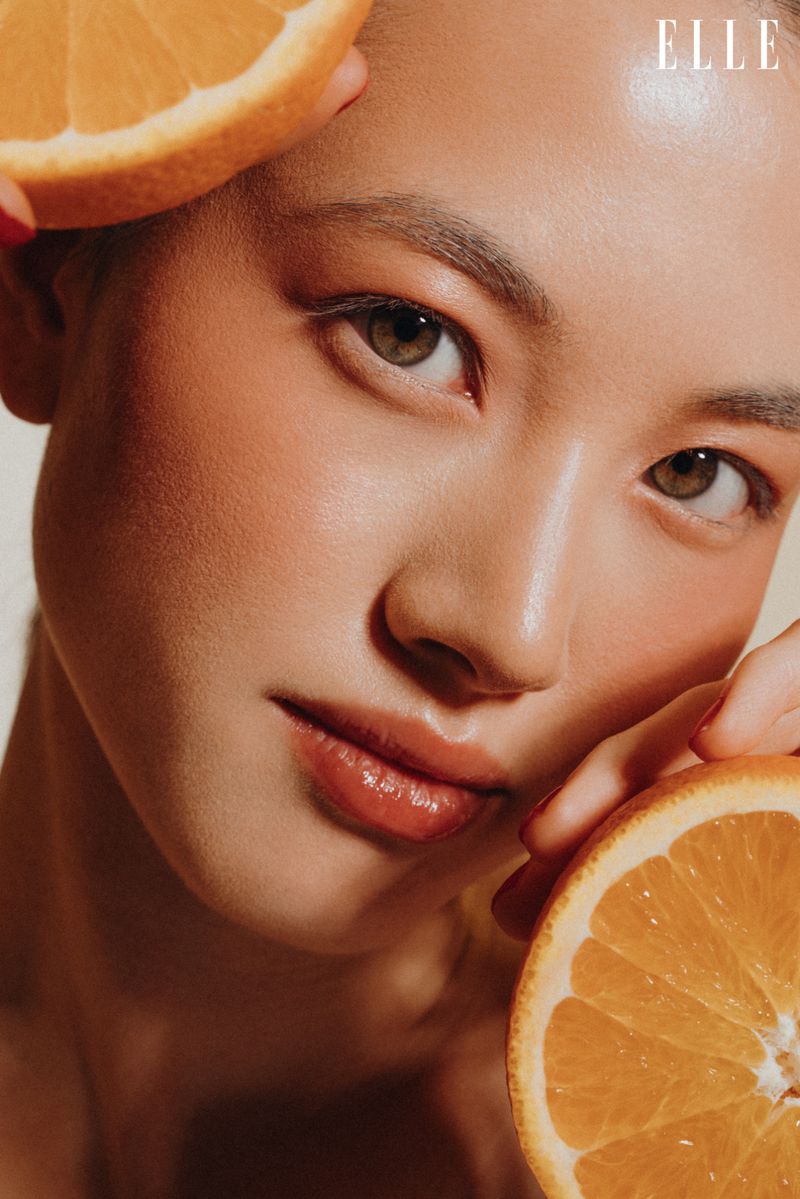 Close-up portrait of an Asian woman posing with orange slices framing her face in a beauty or fashion style with copy space.