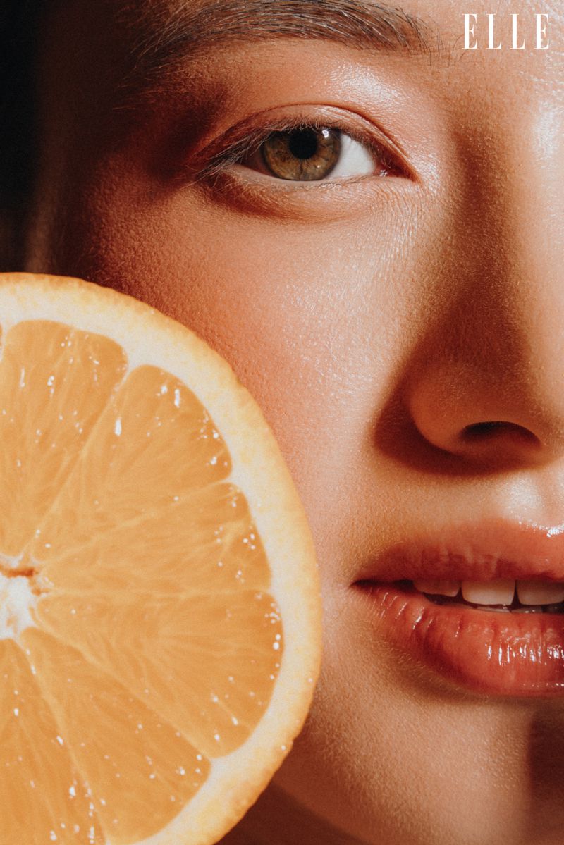 Close-up of an adult woman's face with a slice of orange, showcasing a beauty or skincare theme with natural light and vibrant color.