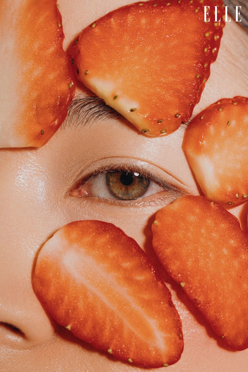 Close-up studio shot of a Caucasian woman's face partially covered with fresh strawberry slices, with the 'ELLE' logo visible.